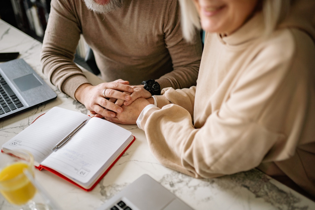 Close up of tow people holding hands sat at a table with a notepad on it