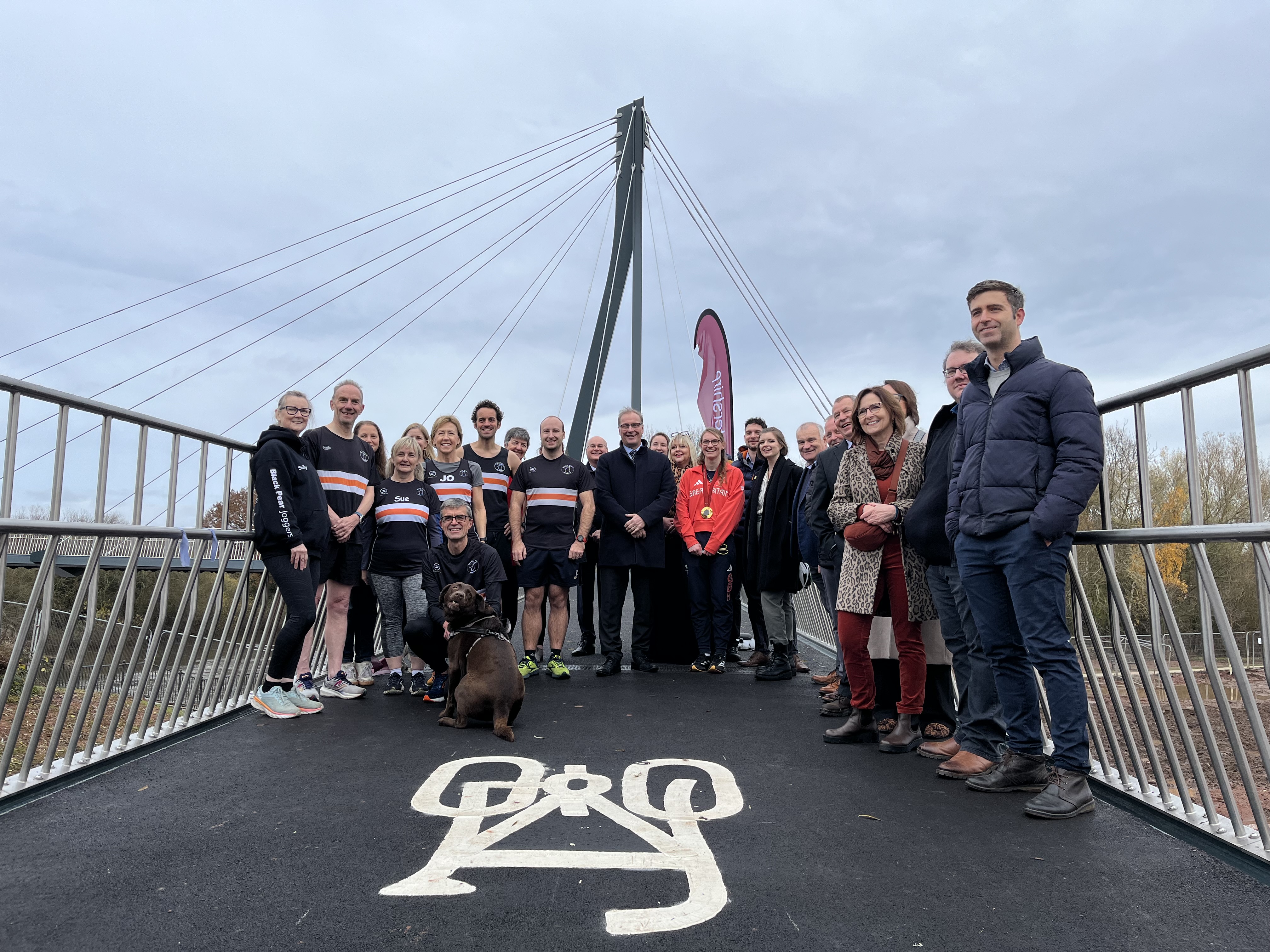 All invited guests stand on the bridge, including representatives from Worcestershire County Council, Worcester City Council, Alun Griffiths Limited, the Worcestershire Local Enterprise Partnership, the Black Pear Joggers, Jacobs, Active Travel England and Friends of Gheluvelt Park alongside Rebecca Redfern MBE.