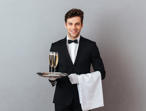 Image of a man in a suit, holding a tray of drinks and a towel over his arm