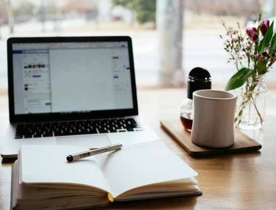 Image of a laptop, open book and pen and a mug